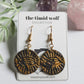 This photo shows a pair of black and gold polymer clay earrings in the shape of a circle. These earrings feature stainless steel hooks, and the design is of the "All-Seeing Eye" is stamped on the circle.